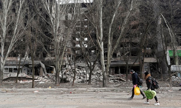 People walk past a destroyed apartment building in Mariupol