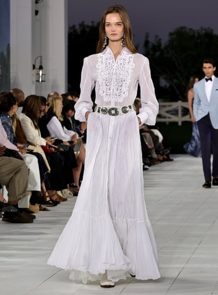 A model walking along the catwalk on a sheer long white dress with a lacey feature front