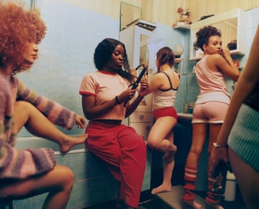 Five women in a bathroom, each performing a different task such as painting toenails or curling hair