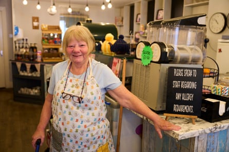 A smiling Tindall, wearing an apron, stands in the tearoom, a hand resting on a counter