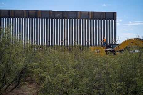 wide view of worker standing on an excavator beside newly installed border wall slats in Big Bend, Texas