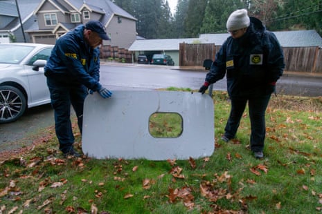 Two officials hold a door plug panel from an airplane in a suburban neighborhood.