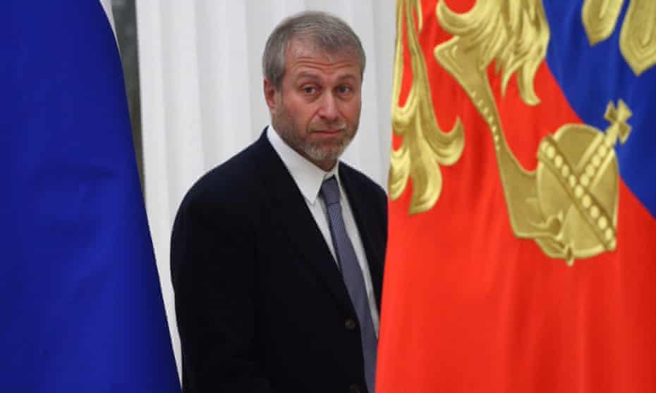 A man smirks at the camera as he walks between two flags at the Russian Kremlin.