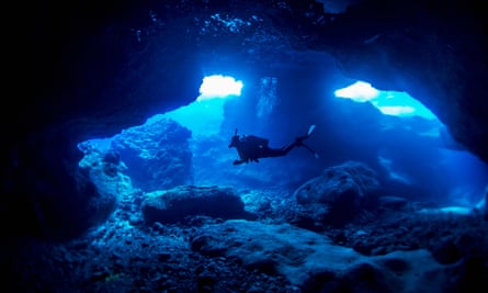 صورة مخزنة لغواص يسبح في كهف ضحل، مع ضوء أزرق يسطع تحت الماء ويضيء التكوينات الصخرية.  صورة جميلة.