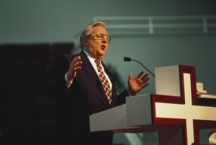 A man in a suit speaks into a microphone from a cross-shaped lectern.