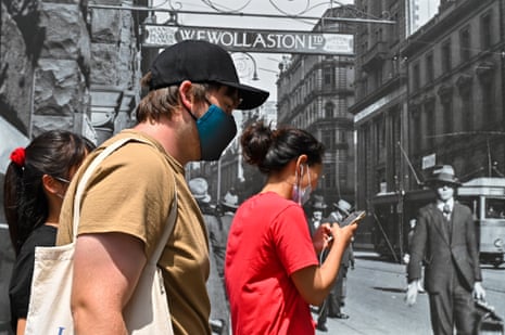 People wearing masks walk in front of a construction site featuring archival images of Sydney