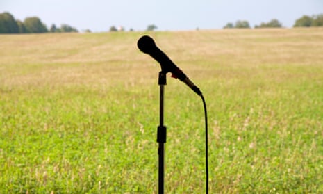 A microphone on a stand silhouetted against a field, with a line of trees on the horizon.
