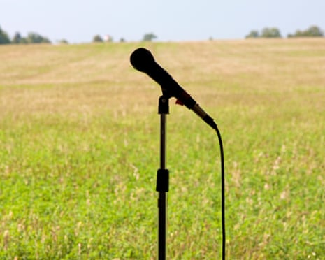 A microphone on a stand silhouetted against a field, with a line of trees on the horizon.