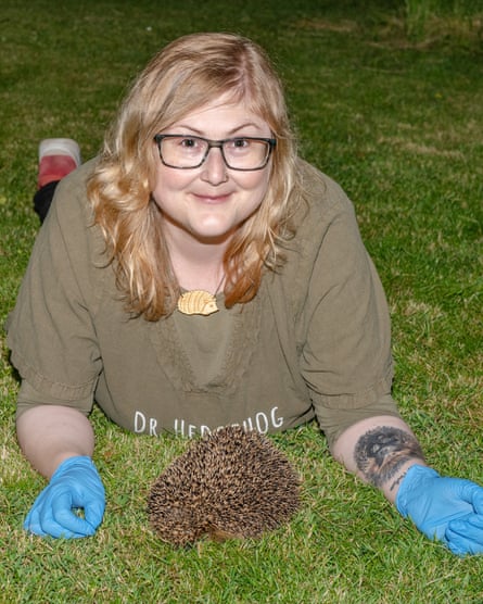 Rasmussen laying on a lawn with a sleeping hedgehog in front of her