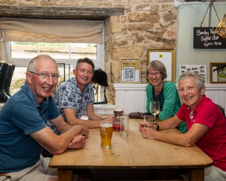 Two men and a woman sit smiling at the camera in a pub.