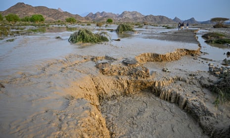 Sudanese people cross a damaged road surrounded by mud and floodwater