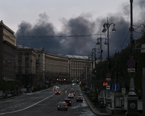 Cars drive along Khreshchatyk Street as smoke rises above buildings in the background following an air attack in Kyiv.