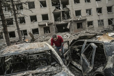 An injured man looks at his burnt vehicle in front of a destroyed building after a deadly strike in the city of Sloviansk.