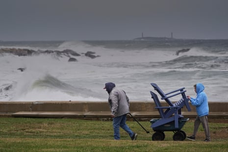 People walk with lawn furniture with an tempestuous ocean in the background.