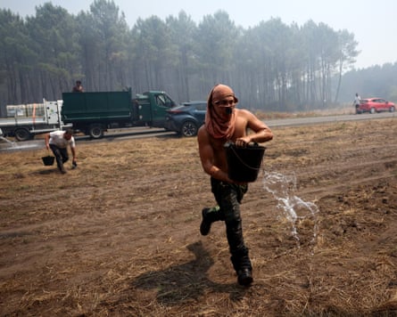A volunteer carries a water bucket and runs from a truck across a dry field. He has a scarf wrapped around his face.