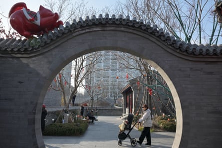 A woman pushes a child on a stroller past an archway with an installation of a cat stretching at the Zhonghai Daji Alley shopping centre in Beijing