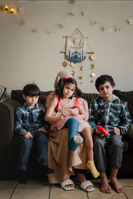 a woman sitting on a sofa with two boys and a girl with her leg in a cast