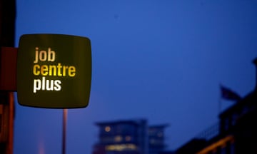 A jobcentre sign lit up with a dark sky and buildings behind