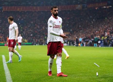 Manchester United's Bruno Fernandes clears the pitch of objects that were thrown.