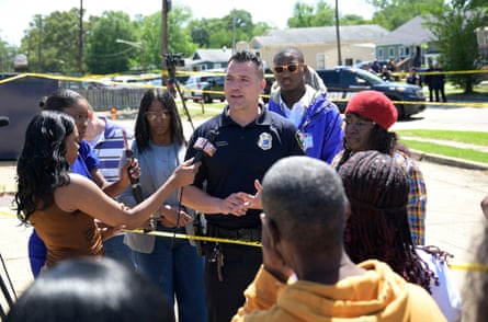 officer speaks to group of people holding microphones outside