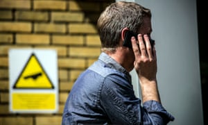 A man on his mobile phone walks past a CCTV sign