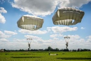 Two paratroopers with white parachutes land in a grassy field