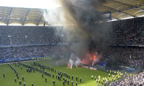 Police officers and security staff stand on the pitch when supporters light fireworks as Hamburg’s proud Bundesliga record came to an end