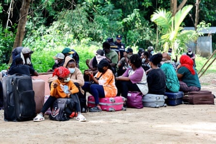 Young African people sit by their suitcases as two Thai police confer in the background