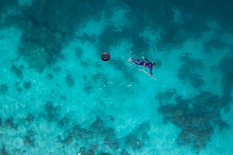 Aerial image of a man spear fishing in a clear shallow blue sea.
