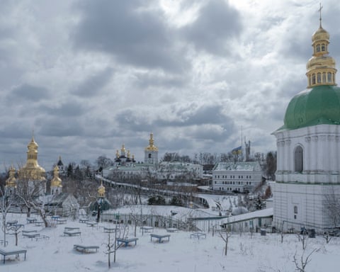 Snow-covered Pechersk Lavra monastery complex with golden-domed buildings and church towers under a dark winter sky