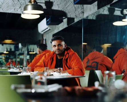 Man wearing orange jacket sits at corner of a restaurant with mirrors behind him.