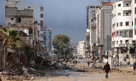 A main street in Gaza City, where destruction is visible on both sides. A few people walk down the centre of the street.