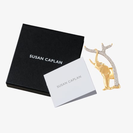 The broche is a gold elephant with the trunk wrapped ina dimante branch laid next to its packaging box.