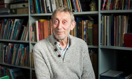 Michael Rosen con un jersey gris y estanterías llenas de libros detrás de él.