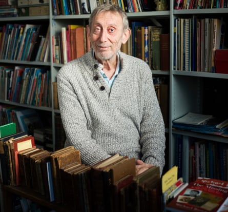 Michael Rosen standing in front of filled bookshelves, a row of old, leather bound books in front of him