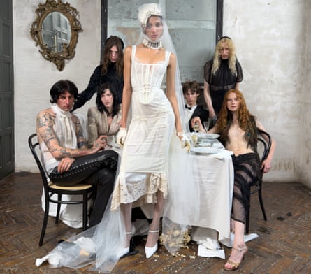 A model wears a white goth-style wedding dress as other models are seated behind