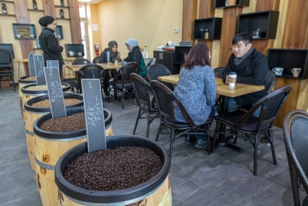 Coffee bean barrels labelled by roast sit before customers chatting at cafe tables