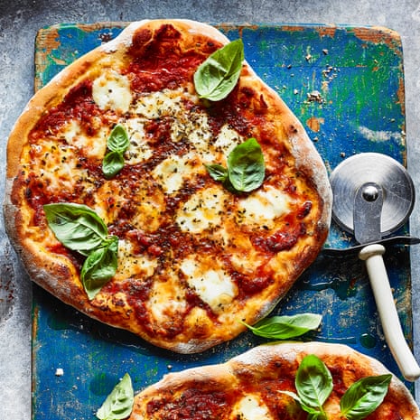 Picture of a homemade pizza margherita on a chopping board with a pizza cutter lying beside it