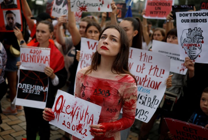 Los manifestantes, incluida una mujer cubierta con sangre falsa, sostienen carteles que condenan el ataque a Olenivka.