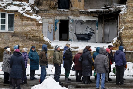People in Horenka queue for food next to a Banksy graffiti on the wall of a ruined building.