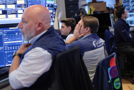 Several traders at stock market screens – one with his head in his hands