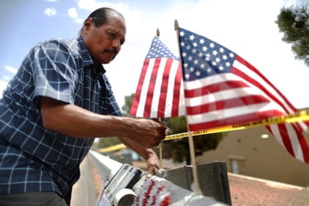 Jose Ozuna installs American flags next to crime scene tape at a makeshift memorial honoring victims outside the Cielo Vista Walmart in El Paso.