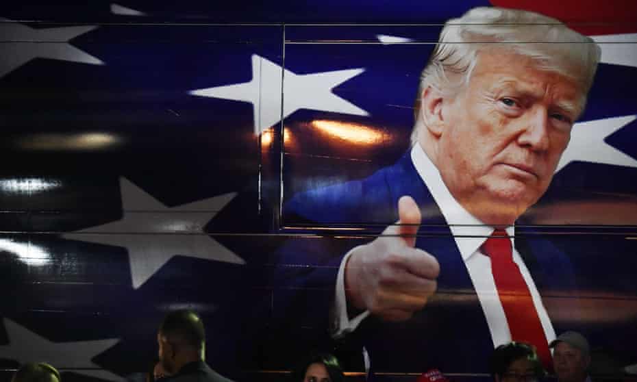 An image of President Donald Trump giving a thumbs up is displayed on the side of a campaign bus at a press conference 