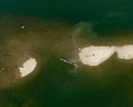 Aerial view of a long rowing boat filled with people in shallow water