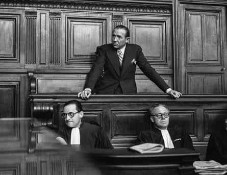 A black and white photograph of French journalist and politician Jean Luchaire, standing in the dock during his trial, behind his two lawyers