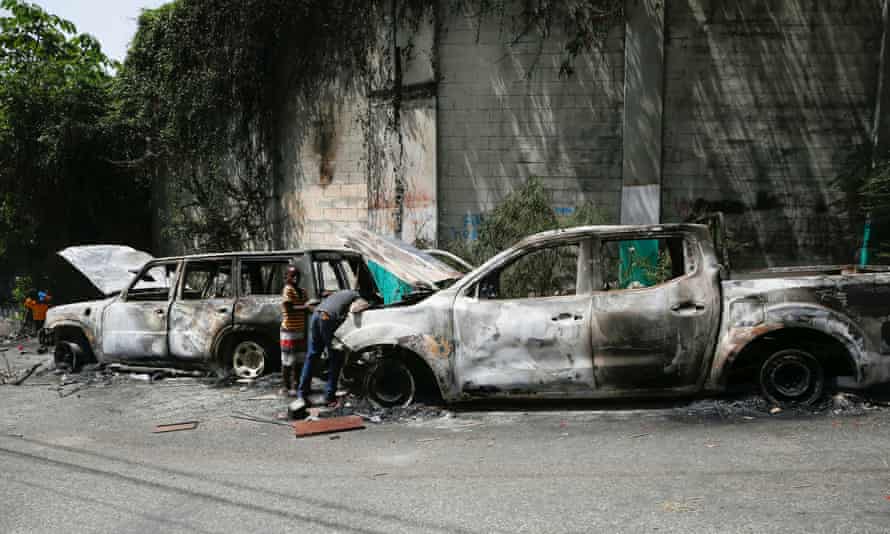 Children look for metal pieces in cars burnt by locals after a firefight between police and the suspected assassins of president Moïse