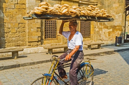 A man carries a huge tray of flatbread on his head while riding a bicycle.