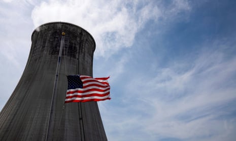 The US flag flies at half mast in front of a coal-fired power plant's cooling tower.