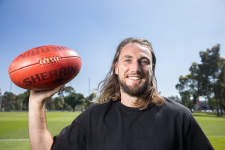 Joel Dwyer holds a football up in a park under a blue sky