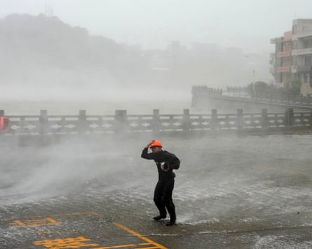 A man holding his hat on while he tries to walk against the wind in driving rain